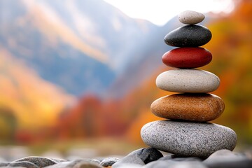 A tranquil stack of colorful stones symbolizes balance and harmony within nature. The backdrop features soft, blurred autumn mountains, creating a serene and peaceful atmosphere.