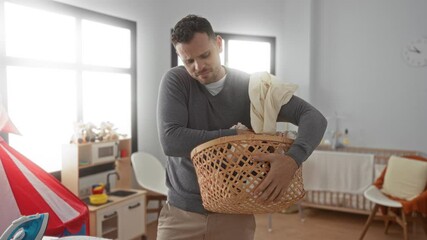 Young man doing laundry in a modern home setting, focused and busy with a full basket of clothes, showcasing daily domestic activities in a bright, tidy laundry room.