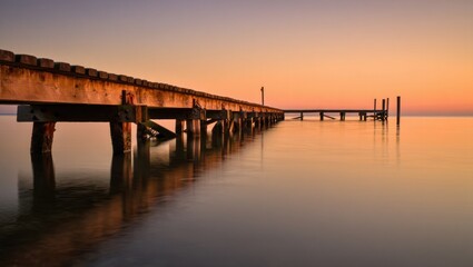 Serene Wooden Pier Reflects Golden Sunset Over Calm Water