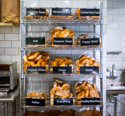 Rack of fresh-baked bagels on display in wire baskets with labels in bagel shop.