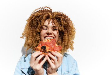 Young woman with curly hair joyfully holding a slice of pizza, showcasing happiness and a vibrant...