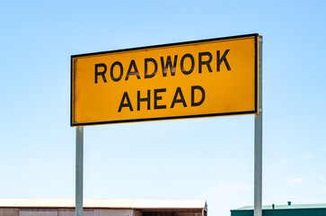 Bright yellow “Roadwork Ahead” traffic warning sign mounted on a metal pole in Australia. The...