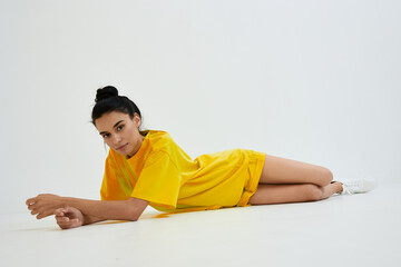 Young woman lying on the floor in bright yellow casual outfit, relaxed pose with neutral white...
