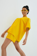 smiling woman in yellow casual outfit and matching glasses posing against white background, joyful...