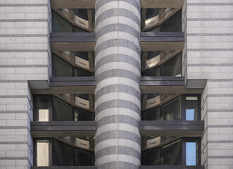 Modern building facade with a central striped cylindrical column and geometric window patterns....