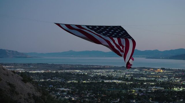 Epic silhouette of beautiful American flag flowing over sparkling valley and lake at dusk - steady drone shot