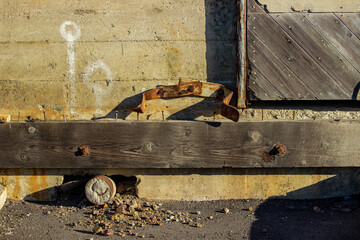 Rusted bracket and wood beam on weathered concrete wall in decay