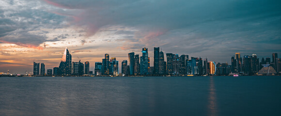 Obraz premium Panorama of Doha, capital of Qatar. View of Doha from the sea. Skyscrapers on a rose and blue background. Modern architecture of Doha at sunset in the evening, view from the sea.