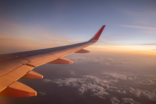 View through window of wing of plane in colorful cloudscape while flying high against sky in sunset.
