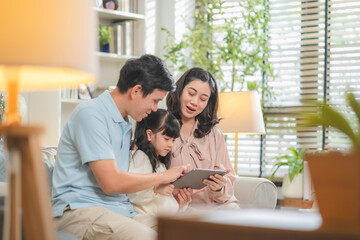Happy Asian family with father mother and daughter using digital tablet laptop for home-based...