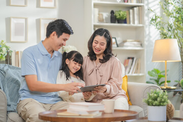 Happy Asian family with father mother and daughter using digital tablet laptop for home-based...