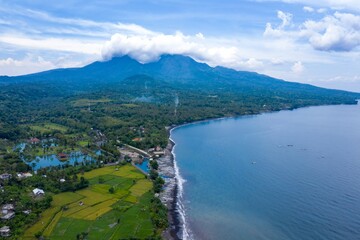 Aerial view of the coastline in Ujung, Bali, Indonesia. Fishing boats line the shore near rice...