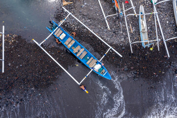 Two fishermen prepare their traditional outrigger boat on a black sand beach in Ujung, Bali,...