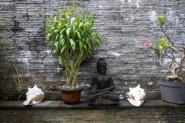 A serene Balinese garden scene featuring a Buddha statue, bamboo plant, seashells, and a flowering...