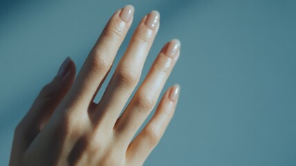 Elegant hand with natural nail polish against a calming blue backdrop