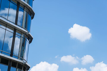 A modern glass office building reflecting the blue sky and white clouds, creating a sleek and contemporary urban aesthetic.