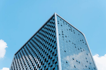 A modern glass office building reflecting the blue sky and white clouds, creating a sleek and...