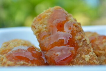 Close-up of crispy fried snack with golden breading, topped with shiny red chili sauce, served on a...