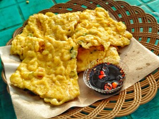 Golden, crispy fried tempeh mendoan (Indonesia), served on a woven plate with chili sauce.
