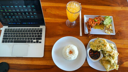 A high-angle, full shot of a wooden table with various food items, including Indonesian fried tempeh, rice, and spicy chicken.