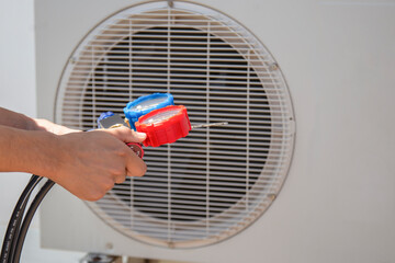 Air repair mechanic using measuring equipment for filling industrial factory air conditioners.	