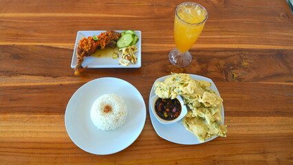 Delicious Indonesian Meal of Fried Chicken, Rice, and Vegetables on a Wooden Table