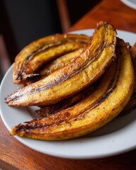 Golden, caramelized plantains on a white plate, served on a wooden table with a cozy background