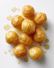 Golden fried dough balls drizzled with syrup, showcasing a delicious dessert on a clean surface