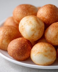 Golden, crispy fried dough balls served on a white plate, perfect for snacking or sharing