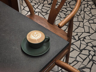 beautifully crafted latte with leaf design sits on green saucer atop dark table, surrounded by...