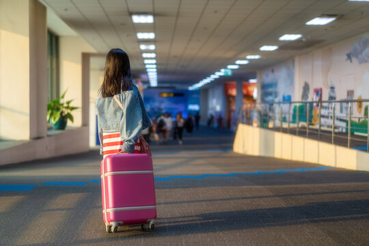 back Asian child on airport to travel or kid girl walking dragging luggage or baggage and pink suitcase to wears denim shirt or jeans fashion on holiday and people journey on winter vacation trip