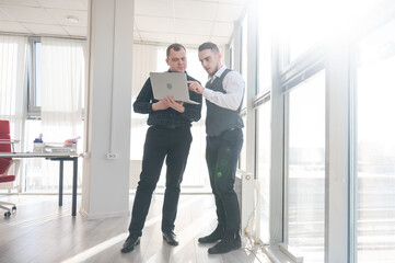 Two Caucasian men looking at a laptop and discussing work. 