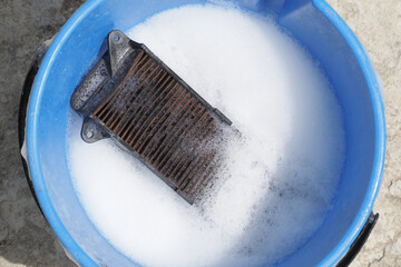 Cleaning old dirty dust air filter from moped in soapy water inside a blue bucket.