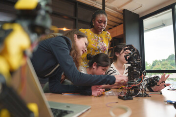 Diverse Teacher helps student girls of different ethnicities learn about robotics arm during a STEM...
