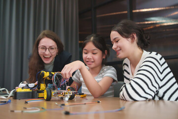 Teacher guiding diverse girl students building a robotic car for STEM project in classroom, smiling and working on electronics together.