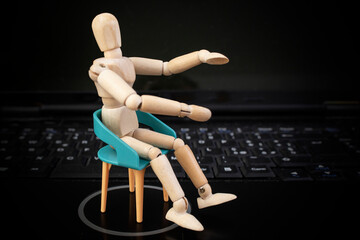 Wooden mannequin standing on chair on black laptop keyboard background