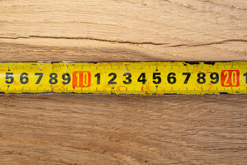 Damaged measuring tape next to a oak wooden board crack in length, abstract repairing backdrop