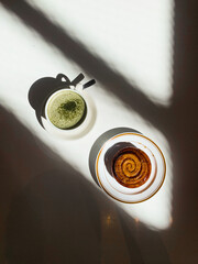 Golden cinnamon roll with glossy glaze served on a plate beside a creamy matcha latte. Bright...
