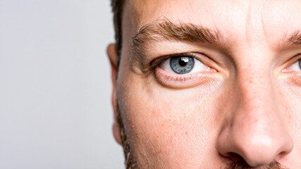 Obraz premium A very close-up shot of a man's face, focusing intently on his blue eye, eyebrow, and stubble/beard texture. The lighting highlights the detail and lines around his eye.