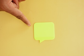 Hand pointing at green sticky note on yellow background