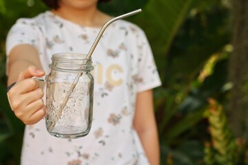 Asian girl show blank glasses of water in her hand with green garden background.Use water-glass and...