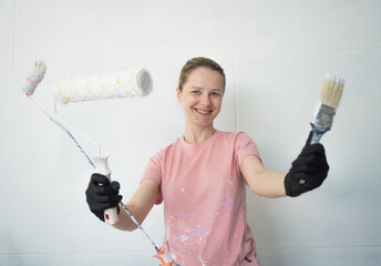 Young woman painting indoors wall with roller using stepladder