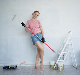 Young woman painting indoors wall with roller using stepladder