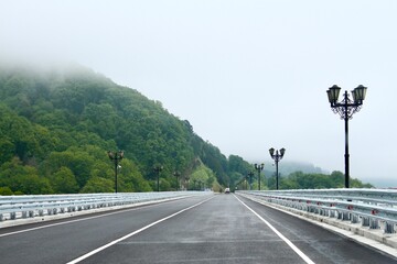 A picturesque road across a bridge high in the mountains where fog hides the peaks and interesting...