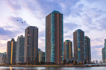 Modern skyscrapers at sunset in Tokyo, Japan. View of high-rise residential buildings along the riverside in the Tsukuda district, with a pastel sky and illuminated windows.