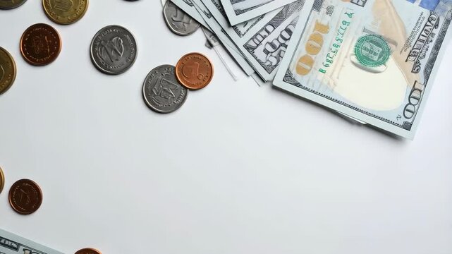Currency collage with hundred dollar bills and a variety of world coins scattered on a white surface, overhead view, financial concept