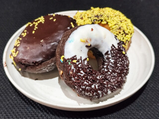 Three delicious donuts topped with sprinkles and various colored glazes, displaying a tempting...