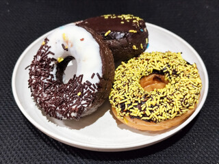 Three delicious donuts topped with sprinkles and various colored glazes, displaying a tempting...