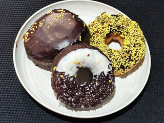 Three delicious donuts topped with sprinkles and various colored glazes, displaying a tempting...