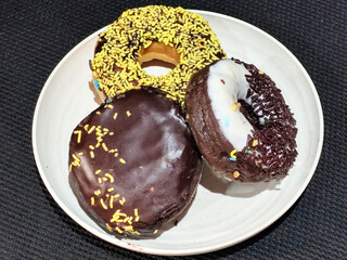 Three delicious donuts topped with sprinkles and various colored glazes, displaying a tempting...